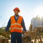 Abbigliamento da lavoro estivo ad alta visibilità: sicurezza, comfort e conformità normativa sotto il sole Builder holding bucket over construction site background